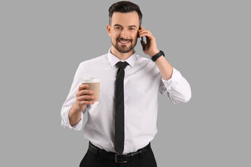 Canvas Print - Handsome businessman with cup of coffee talking by mobile phone on grey background