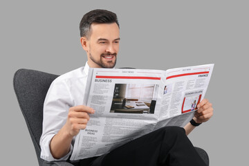 Wall Mural - Handsome businessman reading newspaper in armchair on grey background