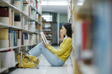 Poster - Student sitting on the floor and reading at library.