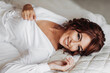 © Vasil - Beautiful young bride in white peignoir lying on bed in hotel bedroom. Final preparations for the wedding. The bride is waiting for the groom. Morning, bride.