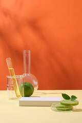 Wall Mural - Front view of lime slices on petri dish, lab glassware containing yellow liquid and white podium on orange background. Empty space for cosmetic of lime extract presentation.