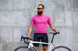 © Georgii - A young cyclist against the backdrop of urban architecture in bright green-black clothes against the background of a red wall with columns, training on a bicycle in the city, walking on a bicycle.