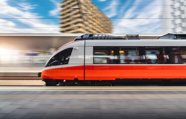 Wall Mural - red high speed train in motion on the railway station at sunset. fast modern intercity train and blu