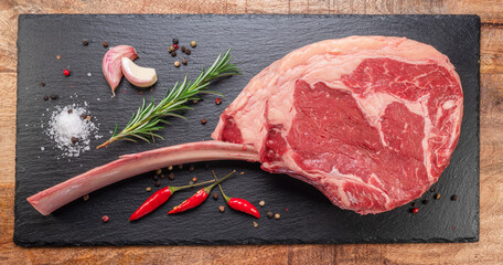 Wall Mural - Raw rib steak with bone or tomahawk steak with seasonings on slate serving plate. Flat lay.