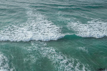 Wall Mural - ocean foamy waves approaching rocky shore. top view.