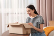 © New Africa - Emotional young woman opening parcel at home. Internet shopping