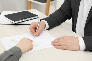 Wall Mural - Woman pointing at document and man putting signature at wooden table, closeup