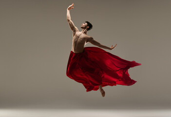 Young, athletic, handsome man, ballet dancer making performance with red silk fabric against grey studio background. Concept of art, classical dance, inspiration, creativity, beauty, choreography