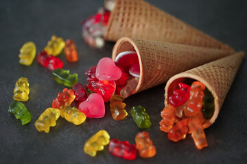 Colorful gummy bears and the hearts by the waffle cones on a black surface