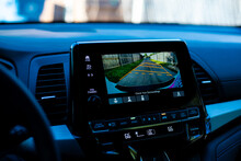 Interior Of Modern Minivan With Blurry Steering Wheel, Large Display Show AC Temperature, Backup Camera Guide Lines, Wooden Fence Along Residential Street Back Alley
