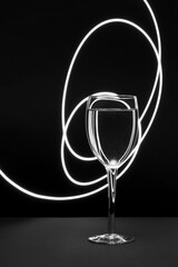 Poster - Vertical closeup of water in a wine glass against a decorative white light on a black studio