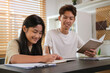 © wattana - Smiling asian male tutor assisting teenage girl doing homework  on table at home.