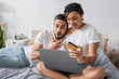 © LIGHTFIELD STUDIOS - amazed african american woman with laptop and credit card near man with open mouth on bed at home.