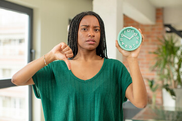 Wall Mural - black afro woman feeling cross,showing thumbs down. alarm clock concept