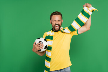 Wall Mural - excited soccer fan in striped scarf holding football isolated on green.