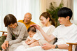 © chachamal - 自宅の居間で赤ちゃんを中心にくつろぐ3世帯5人の幸せで笑顔の家族