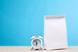 © splitov27 - White lunch bag with alarm clock on the table, blue background. School time