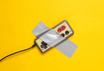 Wall Mural - Retro gamepad fixed with adhesive tape on yellow background. Conceptual pop, video game