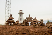 Rocks Balanced In Piles With A Lighthouse In The Background; Prince Edward Island, Canada
