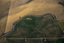 Aerial View Of A Road Winding Through Farmland Divided Into Green And Brown, With An Electricity Transmission Line Running Across; Colorado, United States Of America