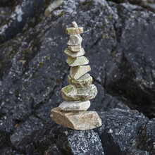 A Pile Of Rocks Balancing On A Black Boulder On Tonquin Beach, Vancouver Island; British Columbia, Canada