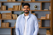 © Ivan - Smiling bearded indian businessman looks at the camera. Young positive male student in library with bookshelves on background. Proud and successful mixed-race small business owner