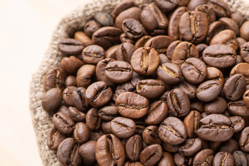 Canvas Print - Dark roasted coffee beans in linen sack against wooden background. Fresh aromatic coffee grain