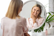© Prostock-studio - Beauty Care. Middle Aged Woman Looking In Mirror At Home And Smiling