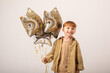 People, joy, fun and happiness concept. Relaxed happy birthday little boy looking cheerful, smiling happily, posing for picture, holding colorful helium balloons
