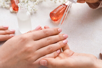 Manicure master applying cuticle oil onto female fingernails on light background, closeup