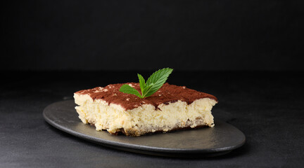 Canvas Print - A piece of tiramisu sprinkled with cocoa, on top of a sprig of fresh mint on a black background