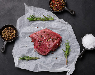 Wall Mural - Raw piece of beef with spices lies on a white piece of parchment paper, top view