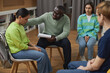 © Seventyfour - Side view portrait of young woman in support group circle sharing story with therapist supporting