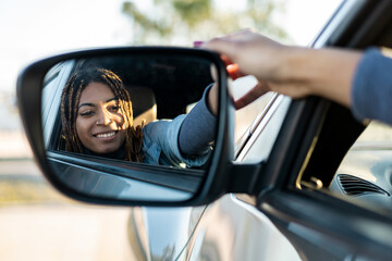 Dark-skinned young girl with braids sitting in a car looking in the rearview mirror while smiling. Testing a new car, novice drivers. Travel concept of African women.