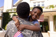 Happy african american boy with flag of america embracing army soldier father outside house
