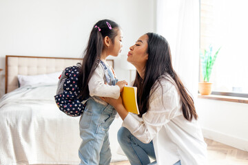 Wall Mural - mother collects asian daughter to school, woman puts on backpack with book to little girl, back to school