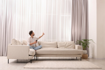 Poster - Man using smartphone on sofa near window with beautiful curtains in living room