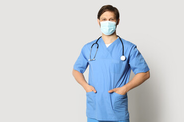 Canvas Print - Doctor or medical assistant (male nurse) with protective mask and stethoscope on light grey background. Space for text