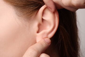 Woman touching her ear on light grey background, closeup