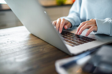 Young adult woman working on her laptop in the kitchen of her home