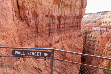 Wooden sign saying Wall Street on Navajo hiking trail in Bryce Canyon National Park, Utah, USA. Selective focus on informational sign. Barren desert landscape with view of natural amphitheatre
