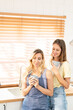 © Wongsakorn - happy lesbian couple holding cups of coffee in kitchen. Couple of lesbian Girls Enjoy coffee at home taking about something. Two young adult beautiful women drink tea in modern kitchen.