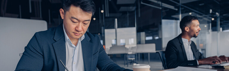 Poster - Focused asian businessman drinking coffee while working with documents in modern office