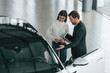 © standret - Talking, holding tablet. Man is showing the new automobile to the woman customer in the car dealership
