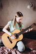 © Анна Молько - the girl is learning to play the guitar at home. learning online