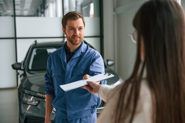 Man giving the document. Young woman is visiting auto mechanic in garage. Repair service