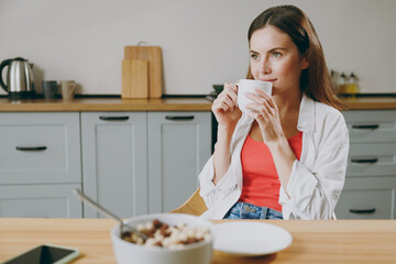 Wall Mural - Young caucasian happy fun european housewife woman wearing casual clothes looking aside in reverie mood drink coffee eat breakfast cooking food in light kitchen at home alone. Healthy diet concept.