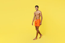 Full Body Side Profile View Smiling Young Sexy Man Wear Orange Shorts Swimsuit Relax Near Hotel Pool Walk Go Look Camera Isolated On Plain Yellow Background. Summer Vacation Sea Rest Sun Tan Concept.