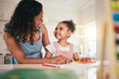 © Clayton Daniels/peopleimages.com - Education, home school and mother and child happy in a kitchen for homework, writing and studying together. Remote, learning and girl with mom smile, bond and excited for fun educational activity