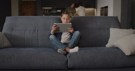 Portrait of Happy Smiling Little Girl Having Fun Using Digital Tablet for E-learning and Playing Games While Comfortably Sitting on Sofa at Home. Female Child Spending Leisure Time With Technology